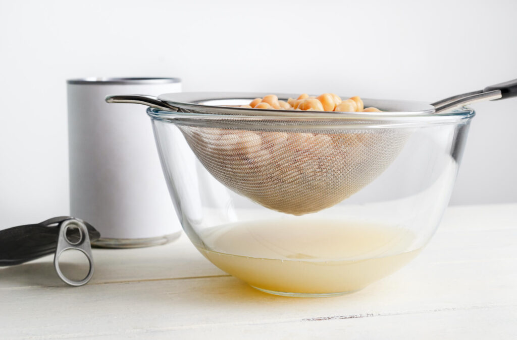 Filtro de metal drenando água do grão de bico aquafaba para um recipiente de vidro