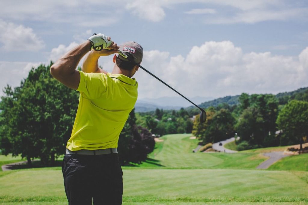 homem balançando taco de golfe em campo de golfe